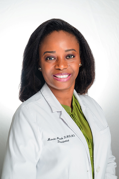 Female dentist in white coat and green top smiling at camera in professional portrait.