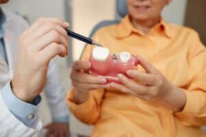Dentist pointing to dental implant model showing tooth replacement options for patient.